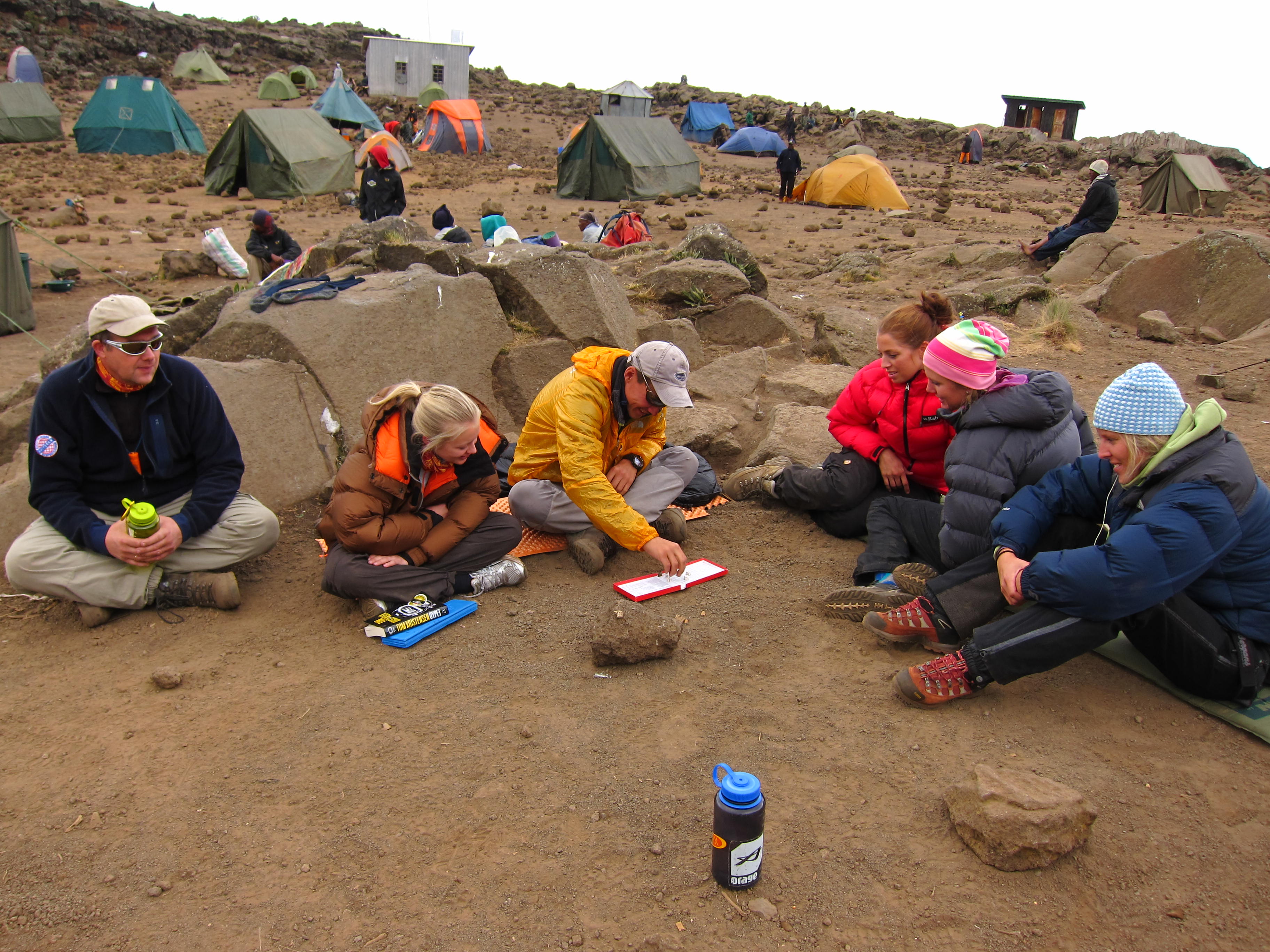 Folk som sitter på bakken i en telt-camp på fjellet