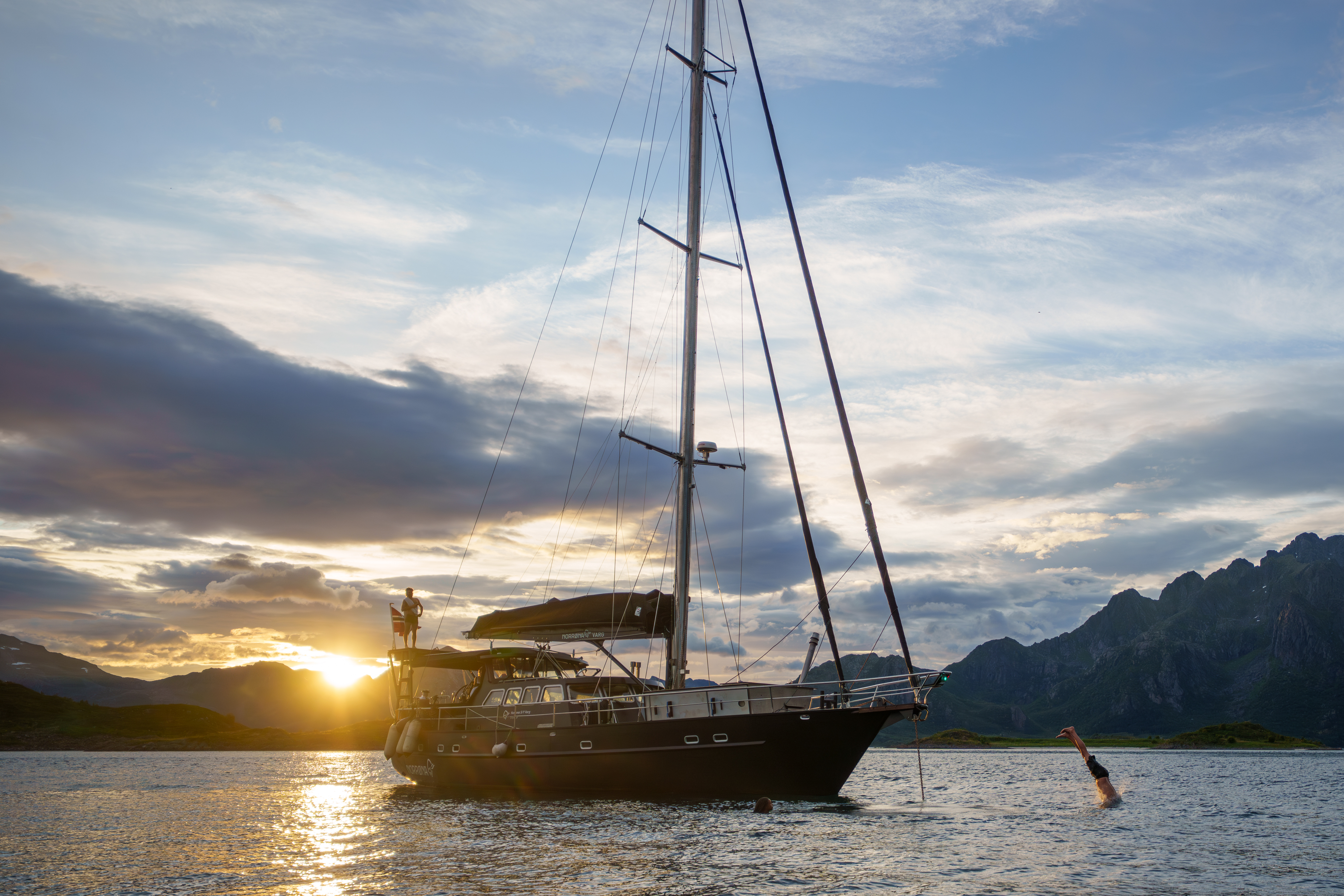 Person som stuper fra en seilbåt under solnedgang