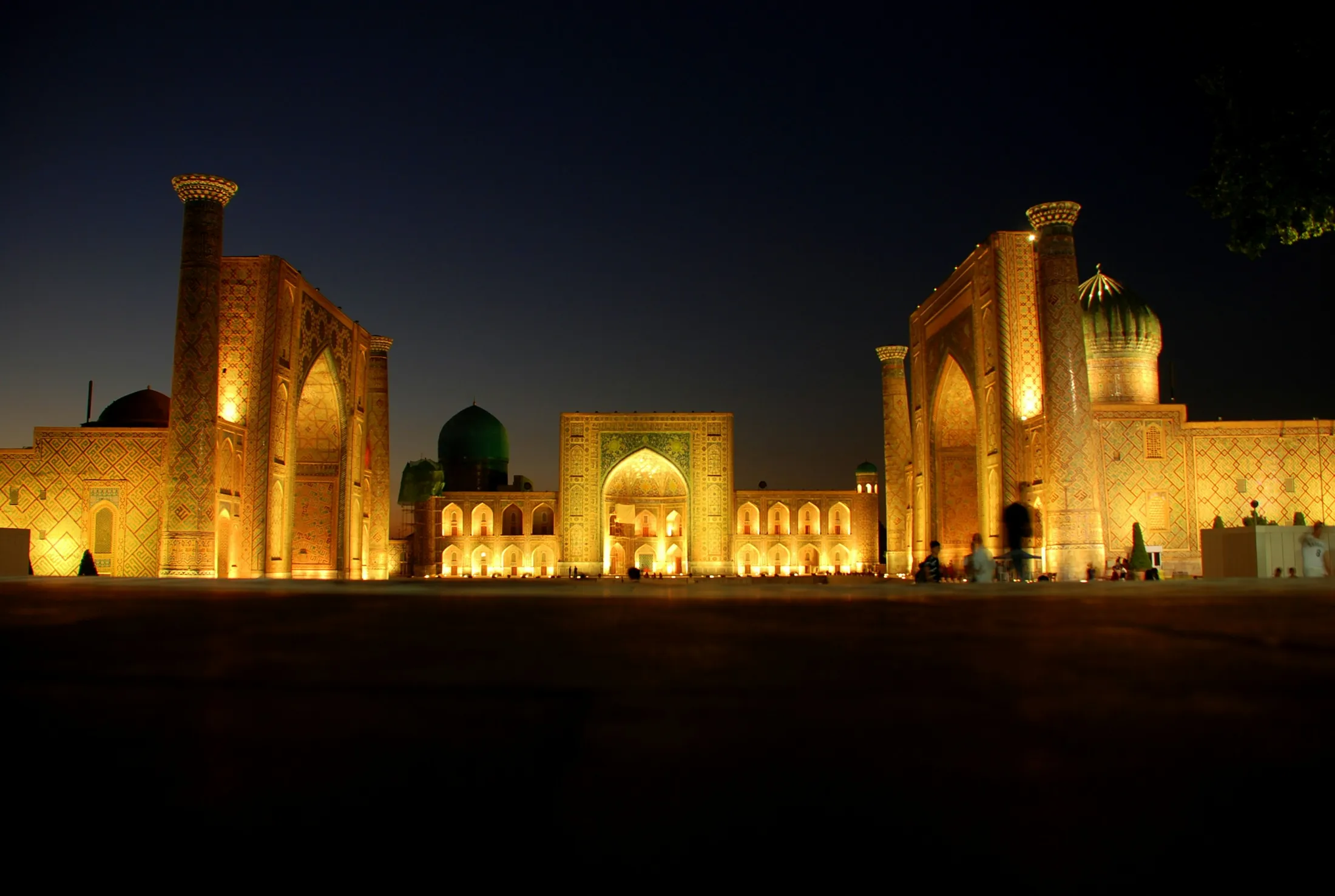 The illuminated ancient madrasahs of Registan Square stand brightly under a dark night sky in Samarkand.