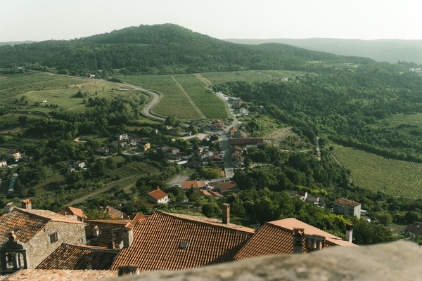 High-angle view of a village nestled in a green valley beneath a rolling hill, with terracotta rooftops in the foreground.