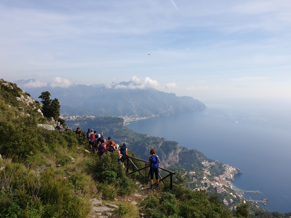 A group of hikers on a mountain trail overlooking the sea and coastline.