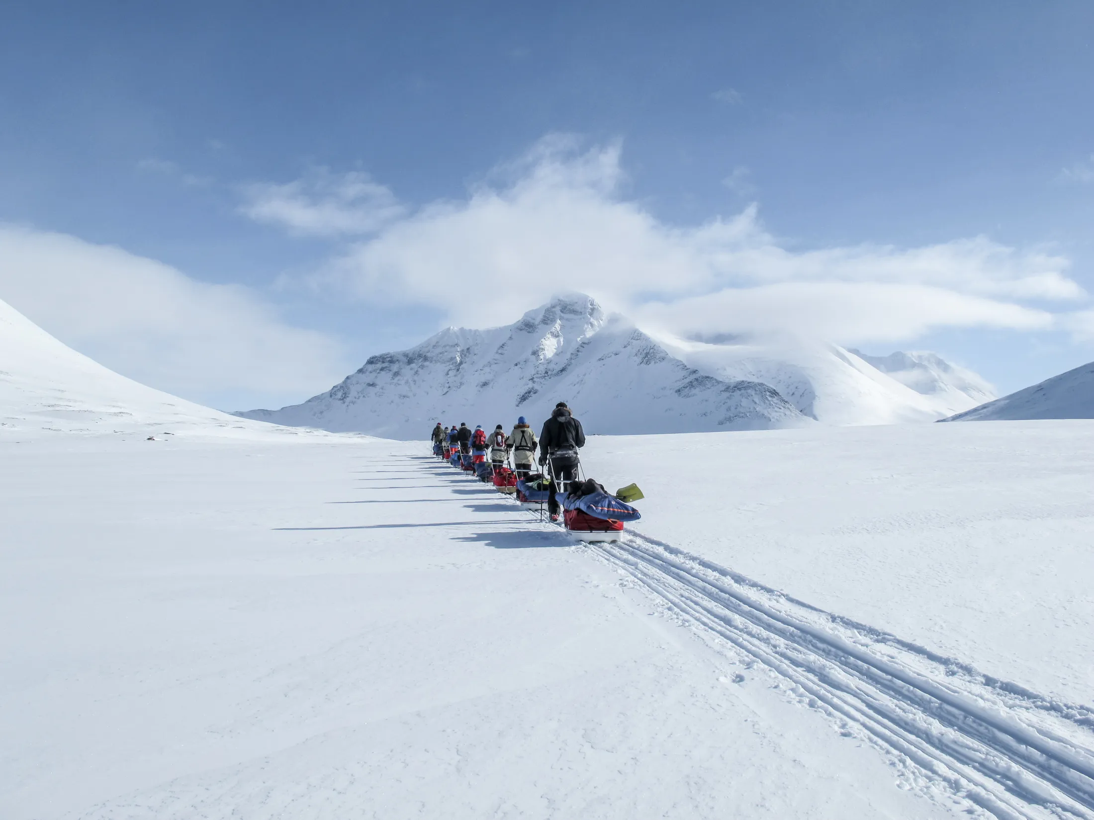 A rope team walking on skis with sleds in the mountains.