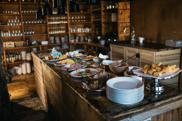A buffet table with food, dishes, and stacks of plates inside a rustic wooden room.