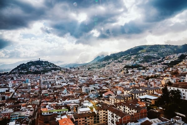 An aerial view of a densely populated city nestled among green hills under a cloudy sky.