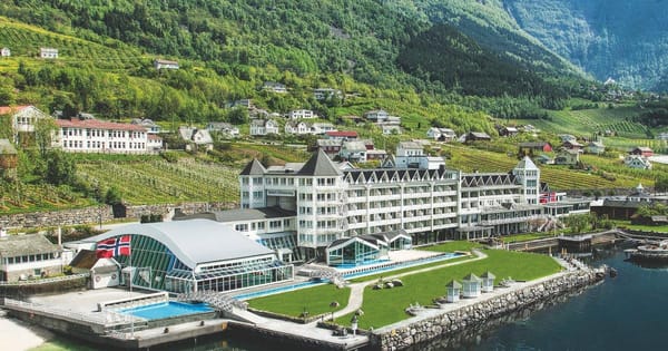 White hotel with swimming pool in the front and the fjord.