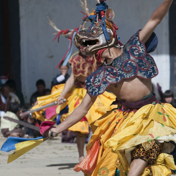A Bhutanese dancer wearing a traditional deer mask and colourful yellow costume performing a dance with a sword.