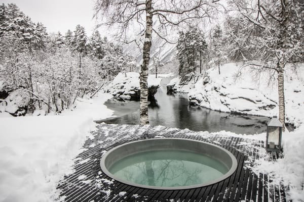An outdoor hot tub in a snowy winter landscape with a river and trees in the background.