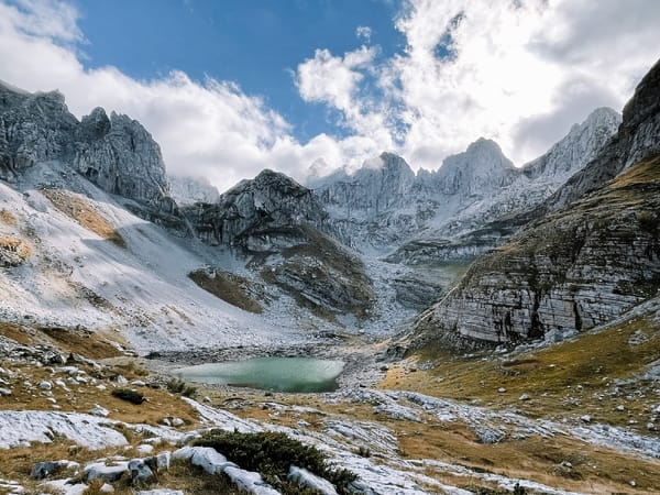 A serene glacial lake nestled in a dramatic rocky valley surrounded by snow-dusted mountains under a partly cloudy sky.