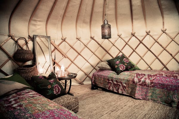 Interior of a cozy yurt with wooden lattice walls, two beds with patterned coverlets, and a hanging lantern.