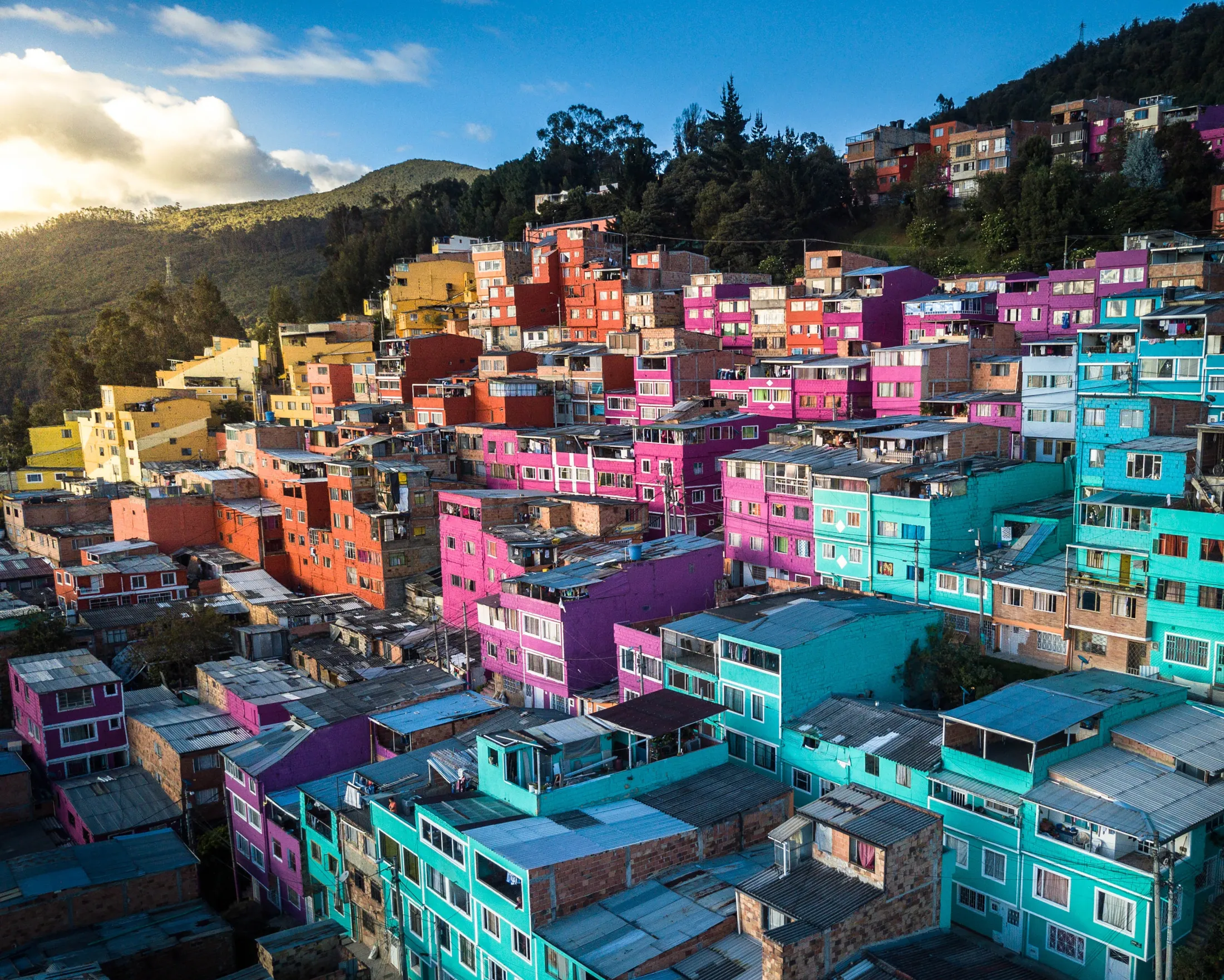 Aerial view of a hillside neighborhood featuring brightly painted colorful houses in shades of pink, blue, and yellow.