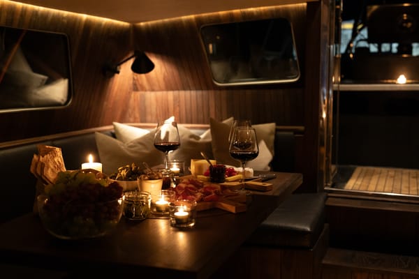 A cozy, dimly lit dining area on a boat, featuring a wooden table set with candles, wine glasses, and food.