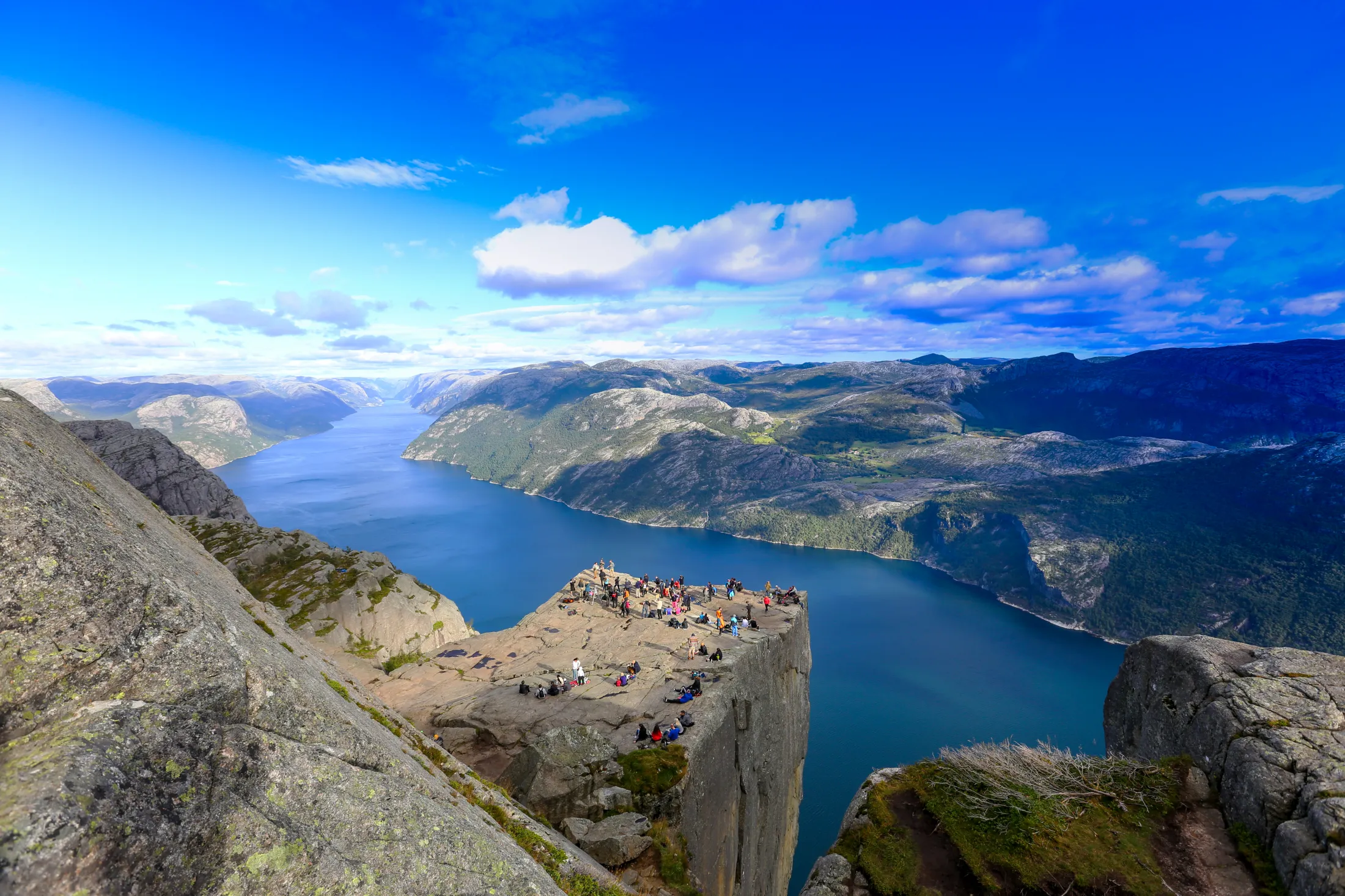 A mountain cliff with people and a blue fjord.