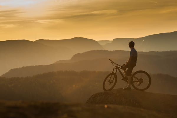A cyclist on a mountain bike overlooking a vast, layered landscape at sunset.