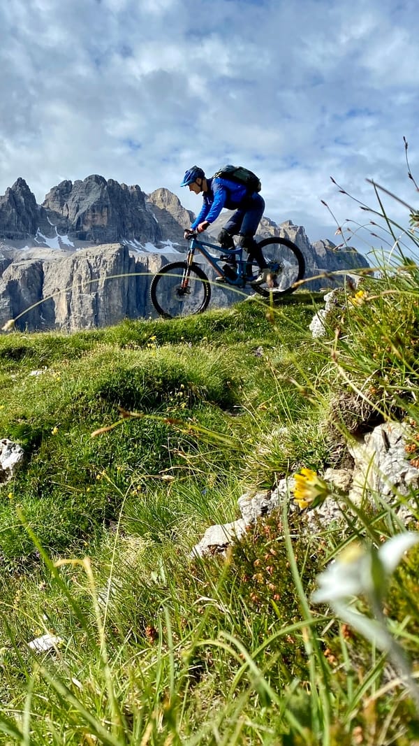A mountain biker riding a trail with jagged peaks in the background.