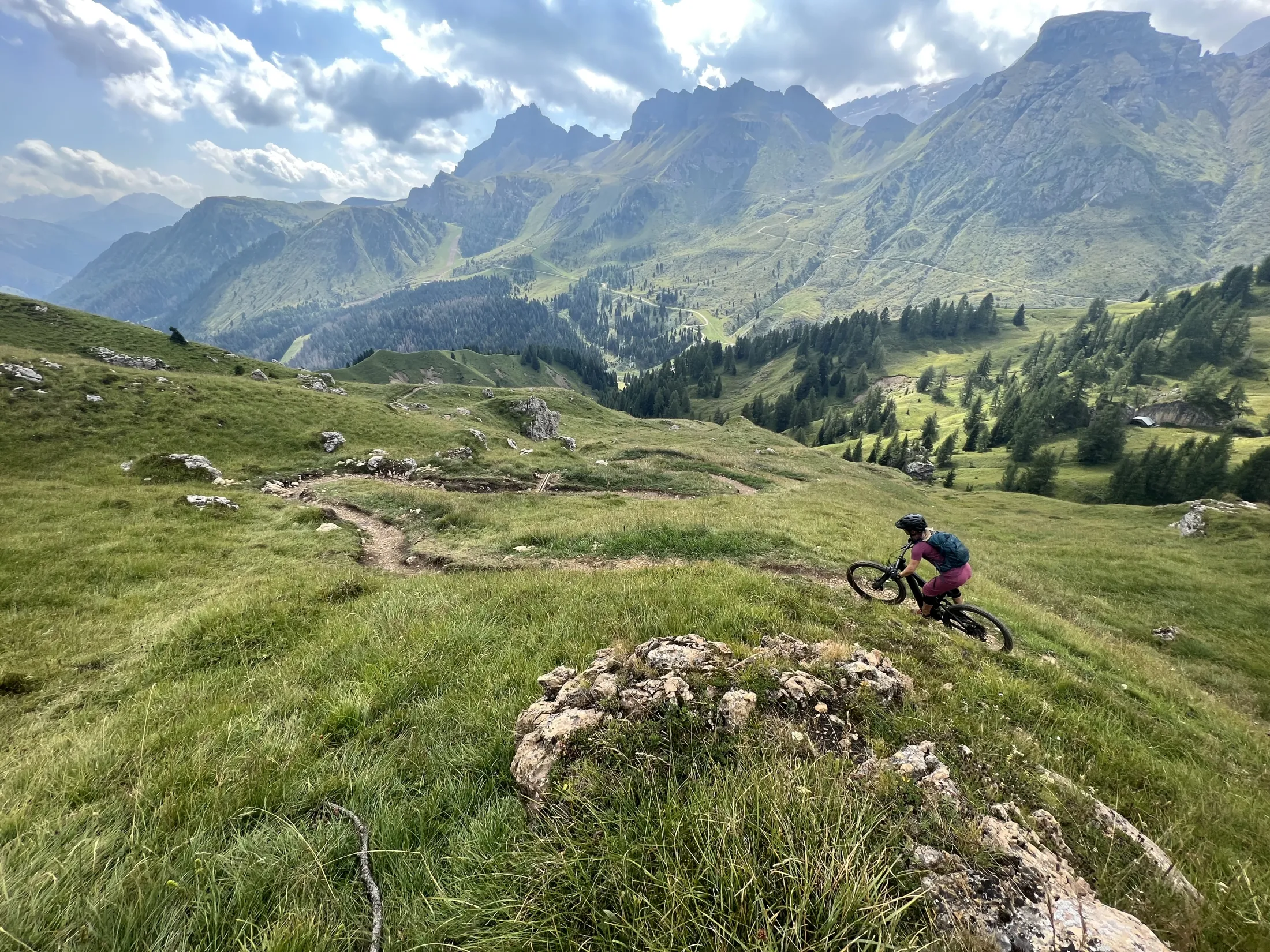 A mountain biker on a grassy hillside with dramatic peaks in the background.