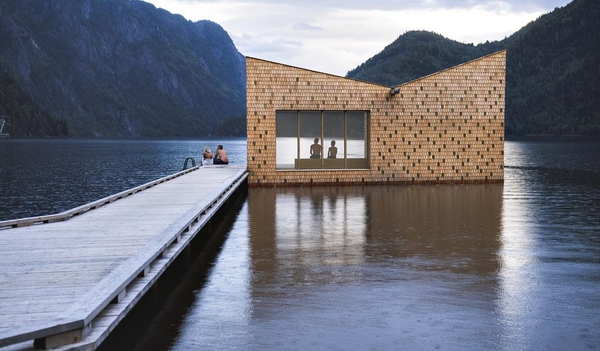 A modern wooden cabin at the end of a long pier on a calm lake, surrounded by mountains.