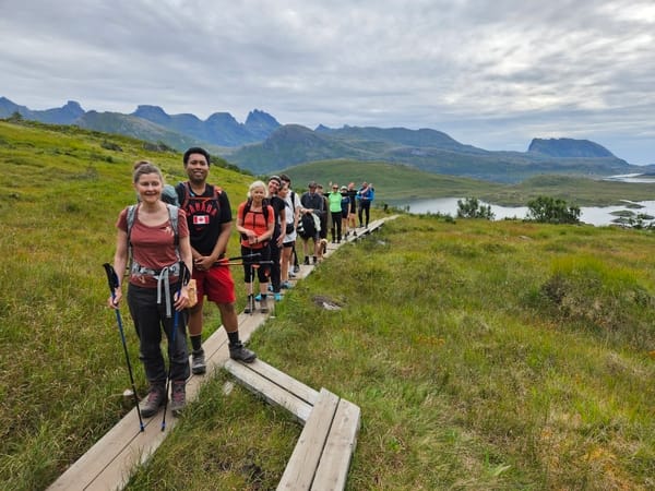 A group of hikers on a wooden boardwalk in a scenic mountain landscape.