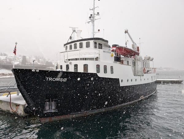 A black and white ship docked at a pier during a snowfall.