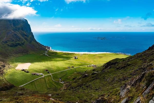 A green valley bordered by steep mountains and the sea, with sunlight illuminating the landscape.