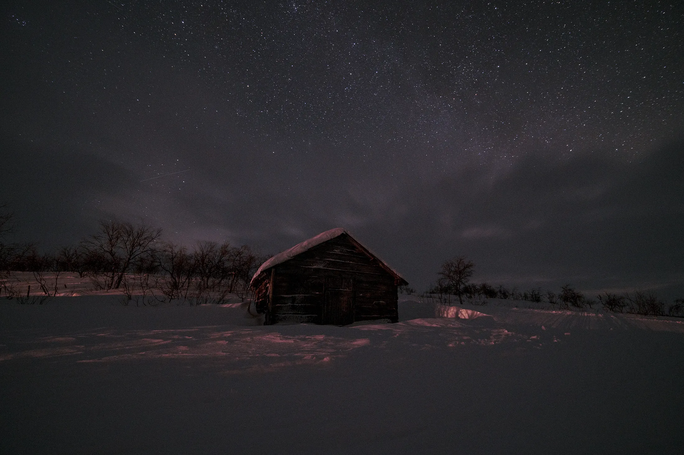 A small cabin in a snowy landscape under a starry night sky.