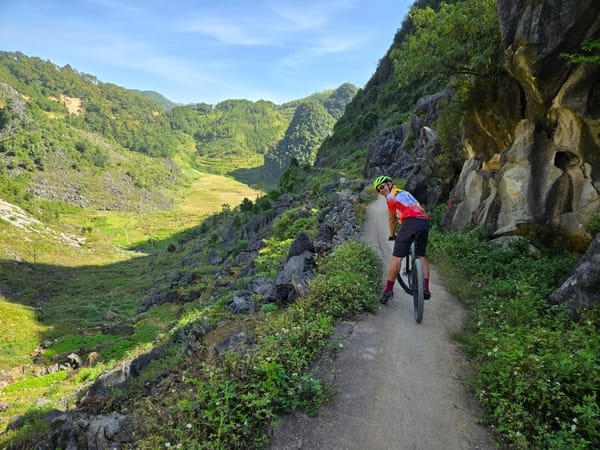 A mountain biker on a narrow path with a lush green valley in the background.