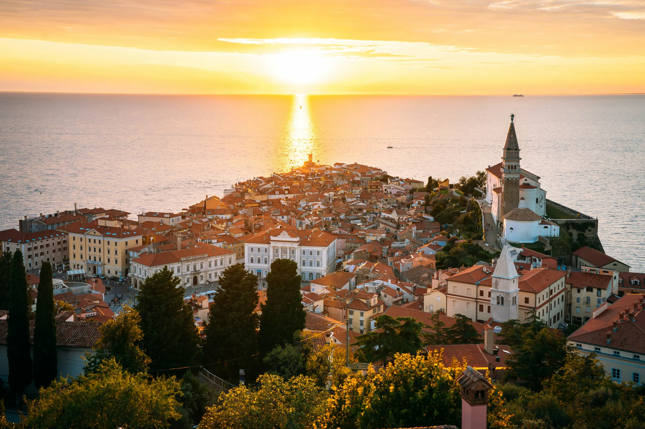 Sunset over a coastal old town by the sea, highlighting historic buildings and church steeples.