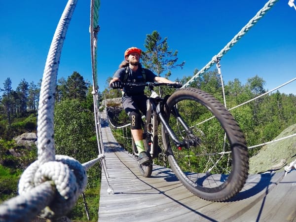 A cyclist riding across a suspension bridge outdoors on a sunny day.