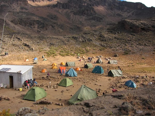 A large campsite with colorful tents and a metal hut set in a rocky mountain valley.
