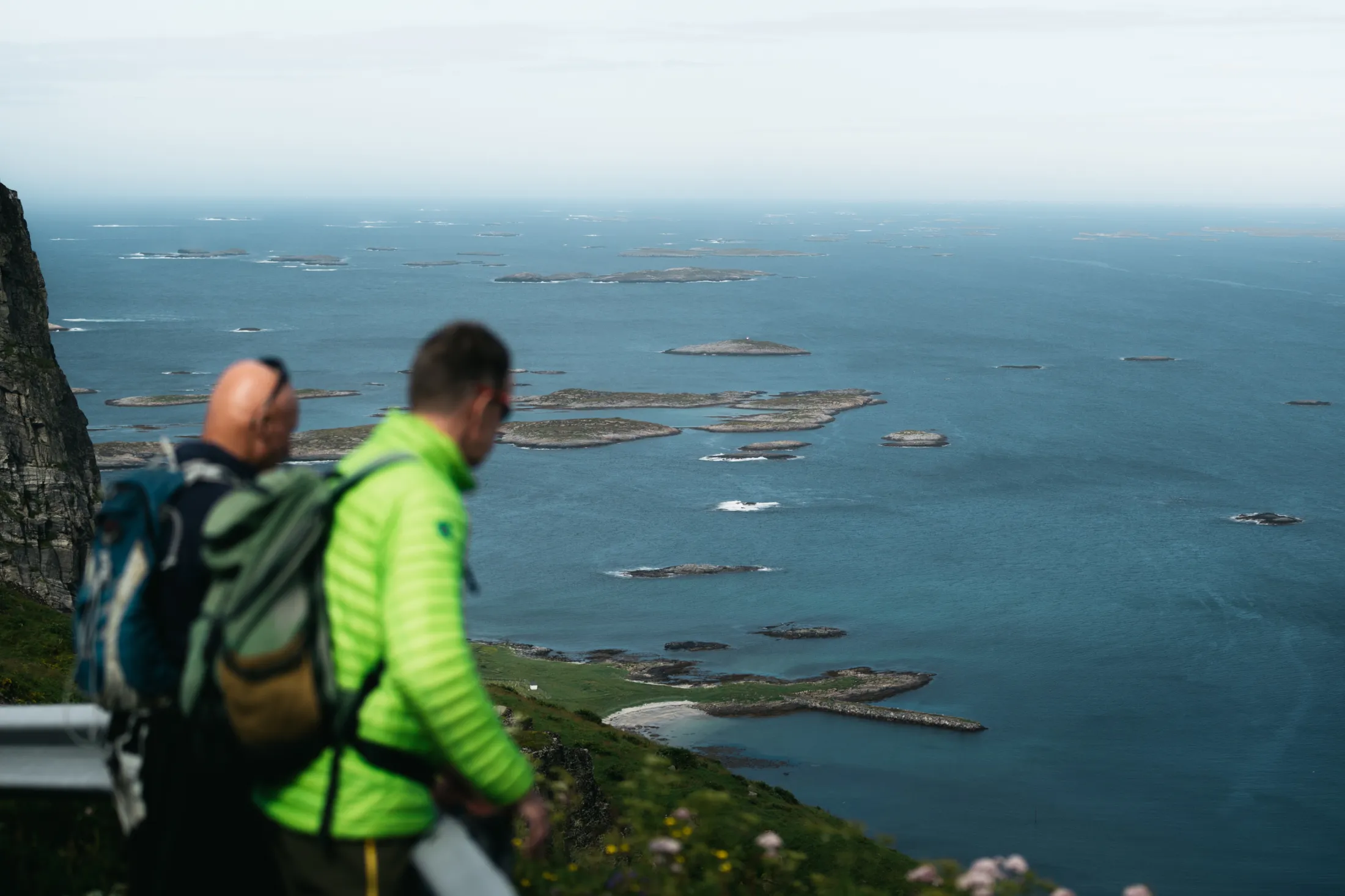 Two hikers standing near a cliff, looking out over the sea and numerous small islands.