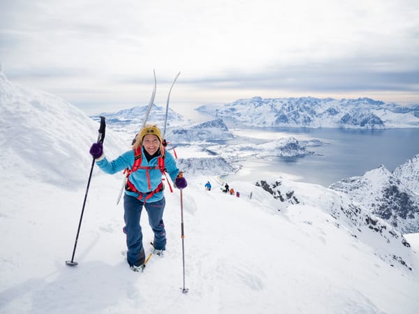 A woman ski touring on a snowy mountain ridge overlooking a fjord.