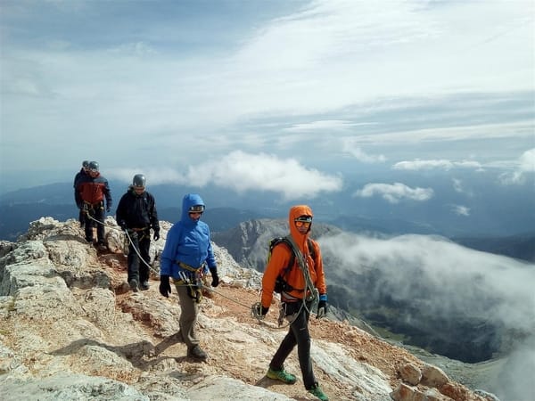 A group of mountain climbers secured together by a rope walk carefully along a high, rocky ridge high above the clouds.