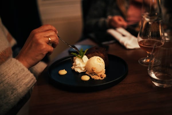 A person about to eat a chocolate dessert with ice cream and whipped cream on a plate.