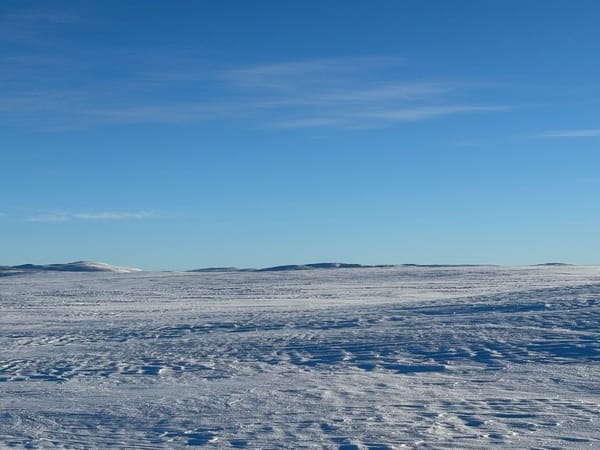 A snowy, flat landscape under a blue sky.
