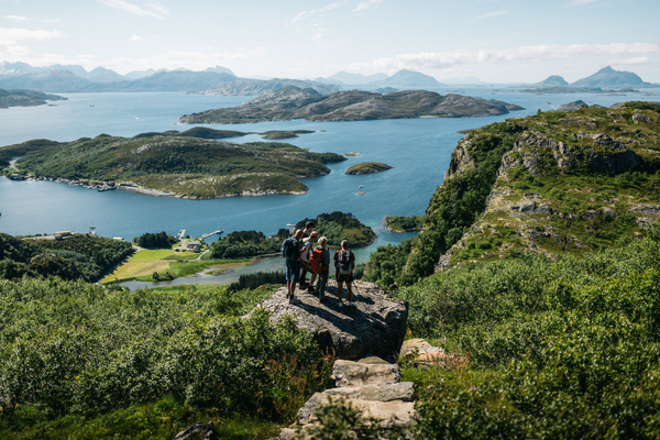 Hikers standing on a rock overlook coastal islands and sea in northern Norway.
