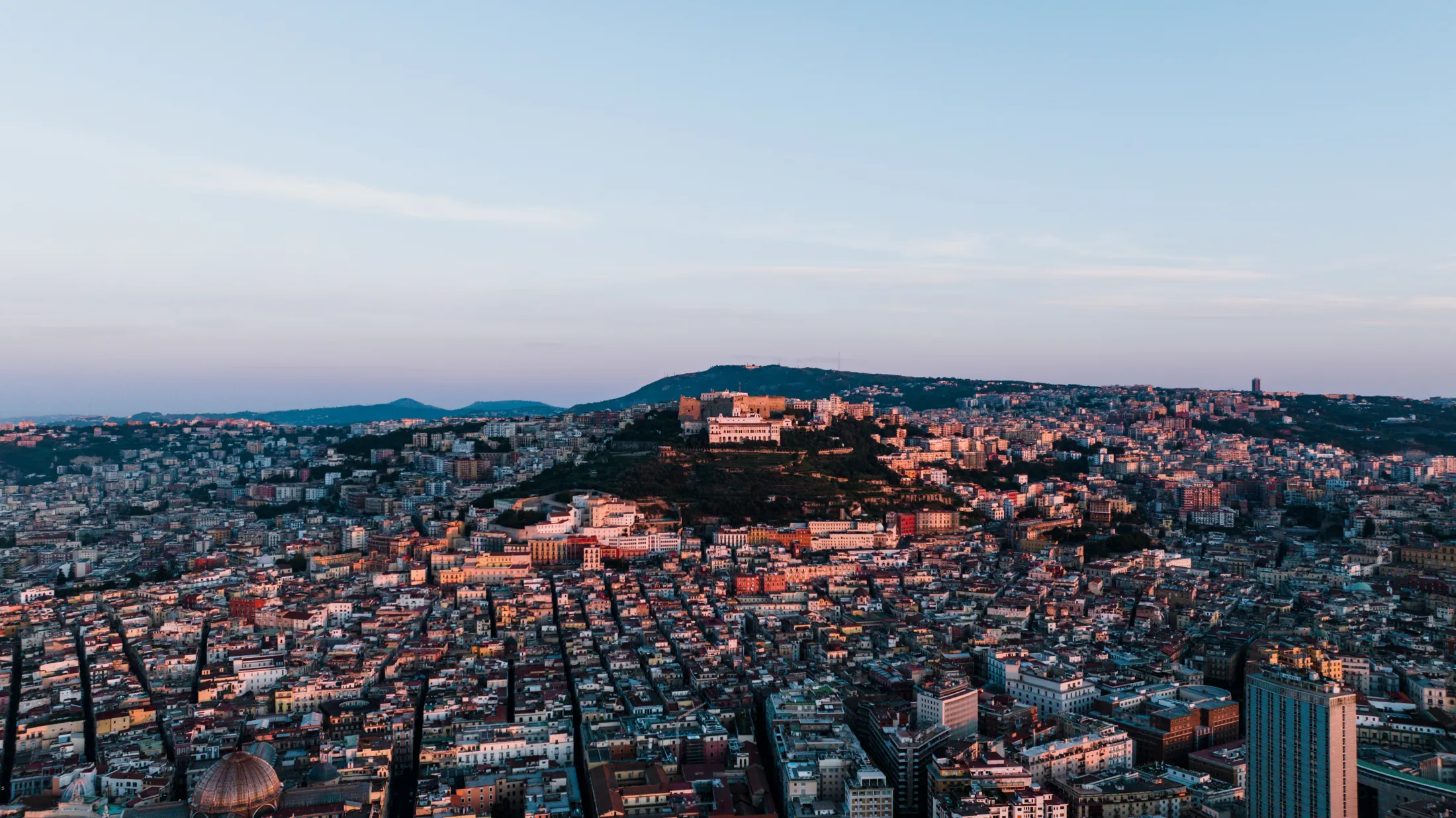Aerial view of Athens and the Acropolis at dusk, with the city lights illuminating the dense urban landscape below.