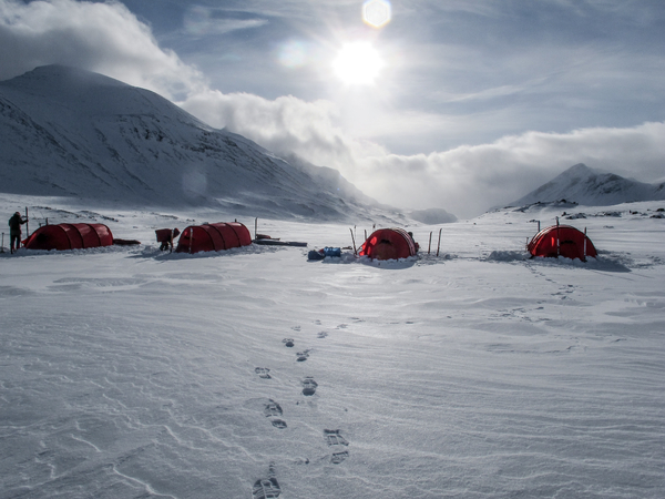 Red tents set up in a snowy mountain landscape under a bright sky with footprints in the foreground.