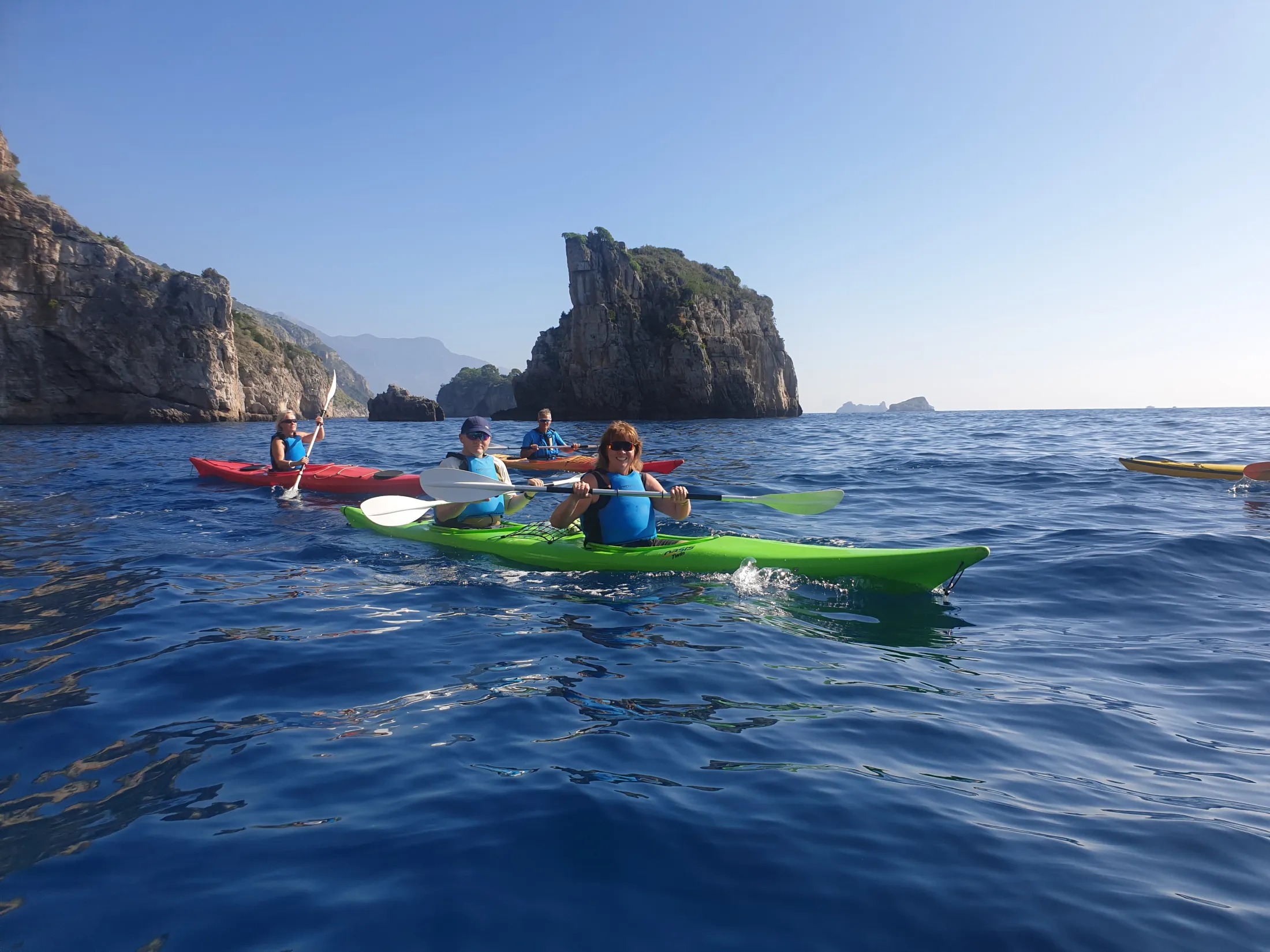 People kayaking on blue sea near rocky cliffs on a sunny day.
