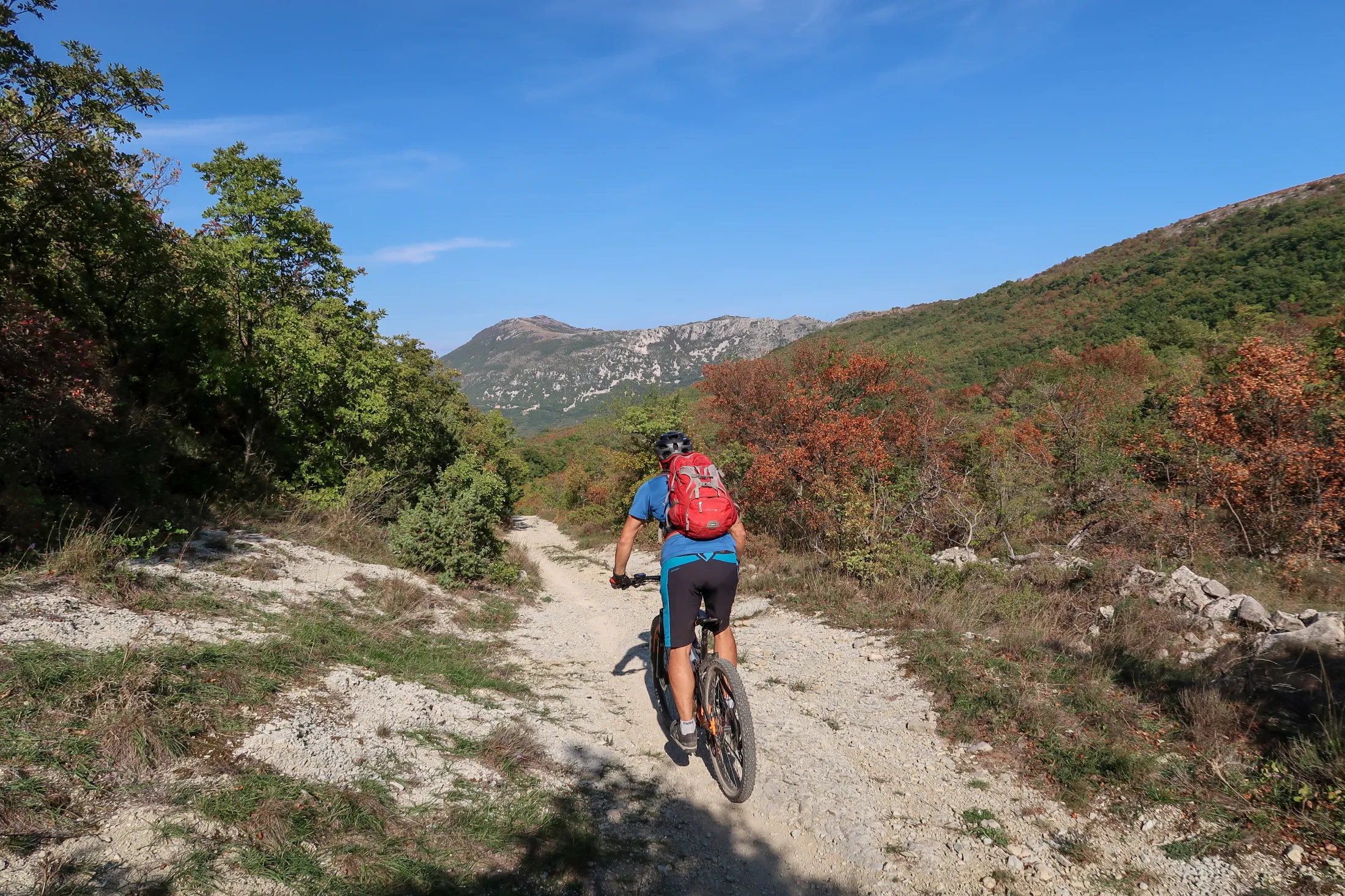 A mountain biker cycling on a dirt trail through a mountainous landscape with sparse vegetation.