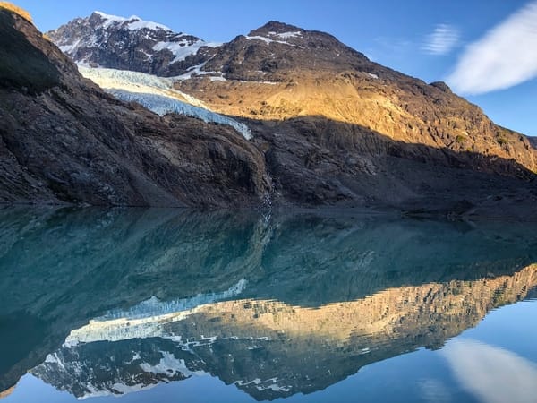 A reflection of a mountain with a glacier in a clear turquoise lake, under a blue sky.
