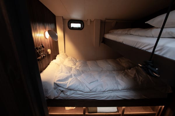 A compact cabin with two bunk beds with white sheets and duvets, illuminated by a warm wall light.