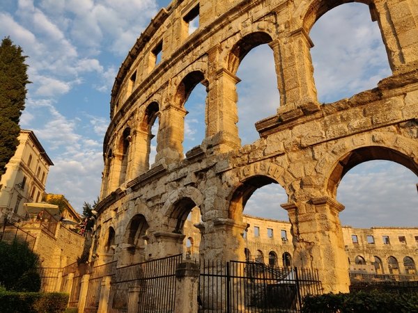 A view of the ancient Roman amphitheater in Pula, Croatia, with stone arches lit by the sunset.