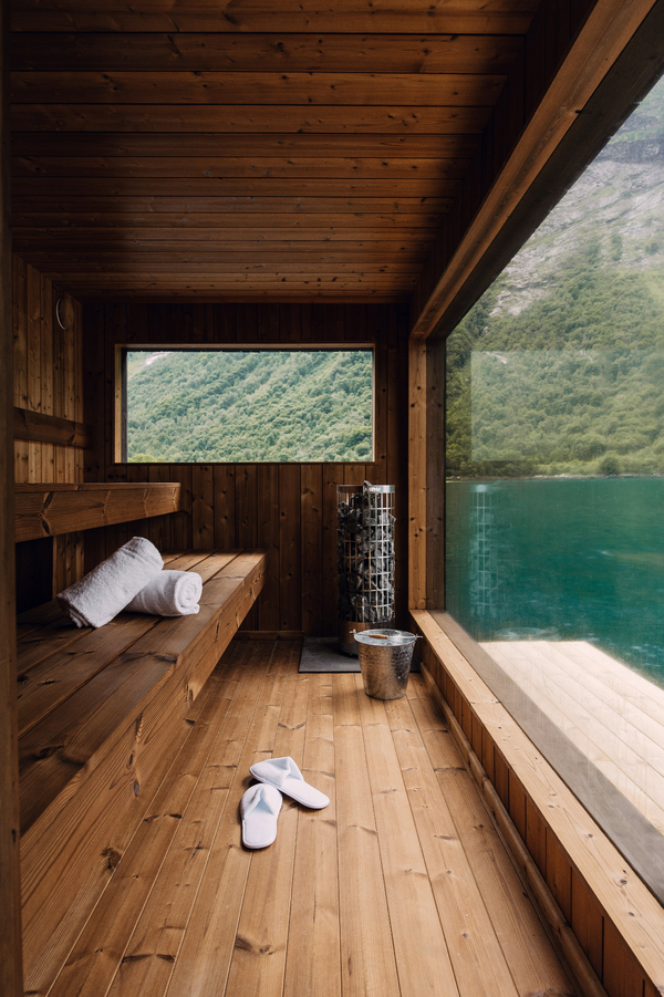 Interior of a modern wooden sauna with large windows offering a scenic view of a fjord and mountains.