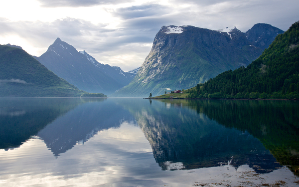 Calm water reflecting mountains and sky under a cloudy sky.