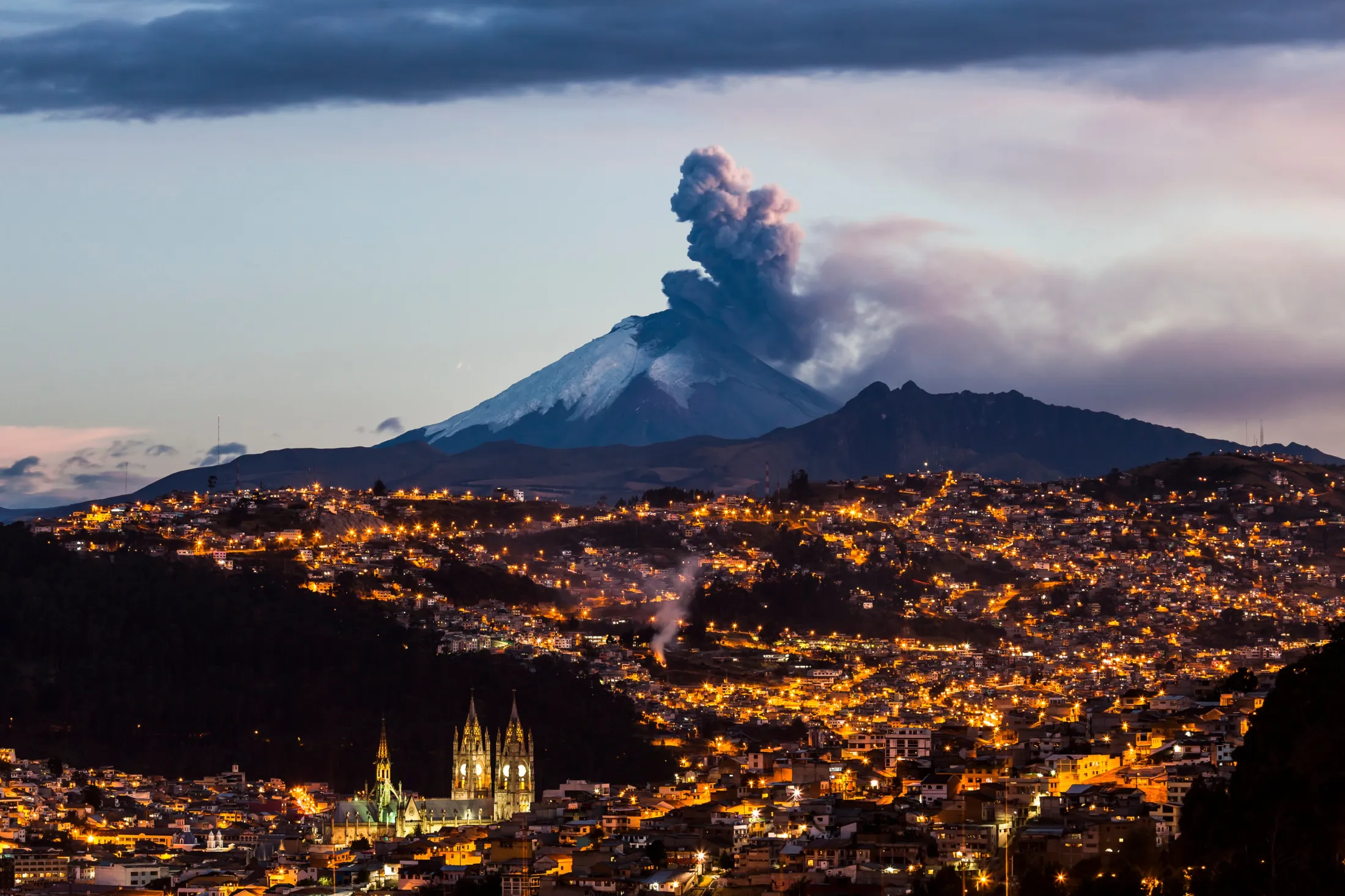 A volcano in the evening with a city in front of it.