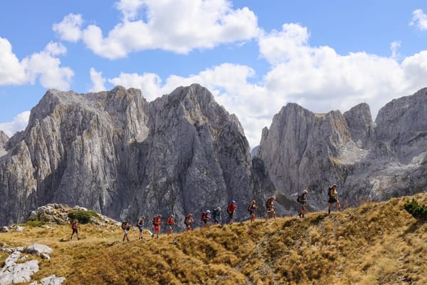 A group of hikers walking on a mountain ridge with rugged peaks in the background.