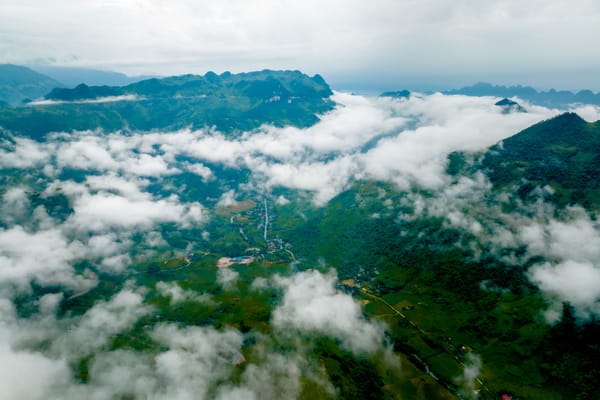 Aerial view of lush green mountains partially covered by low-hanging white clouds.