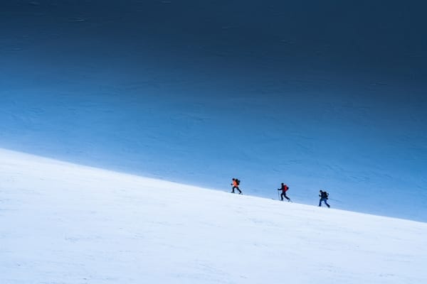 Three people walking on a snowy slope under a blue sky.