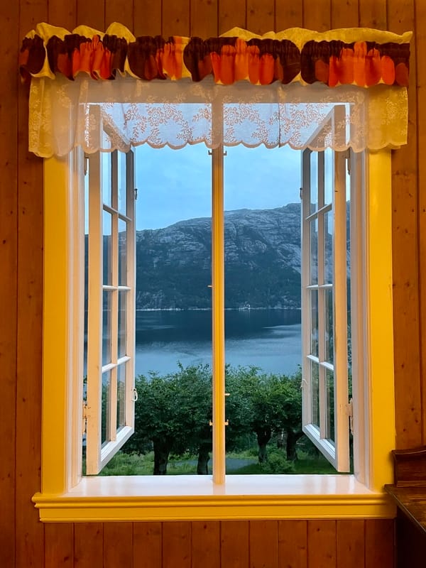 A open window in an old house with the view to fruit trees and the fjord.