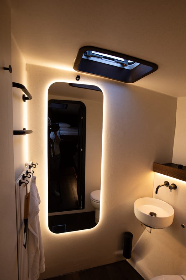 A modern sail yatch bathroom with a backlit mirror, sink, and skylight.