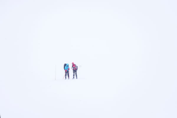 Two people in colorful jackets standing in a vast, white snowy landscape.